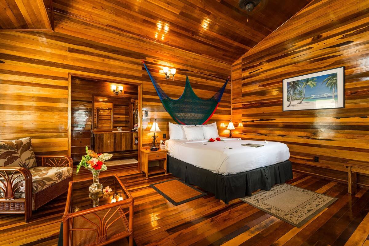 Ein Holzhütten-Zimmer mit einem Bett, einer Hängematte, einem Esstisch und einem Stuhl.