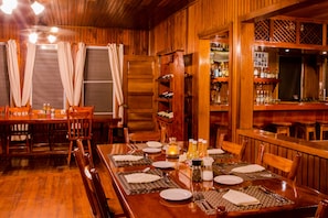 A wooden dining area with a long table set for a meal, surrounded by chairs.