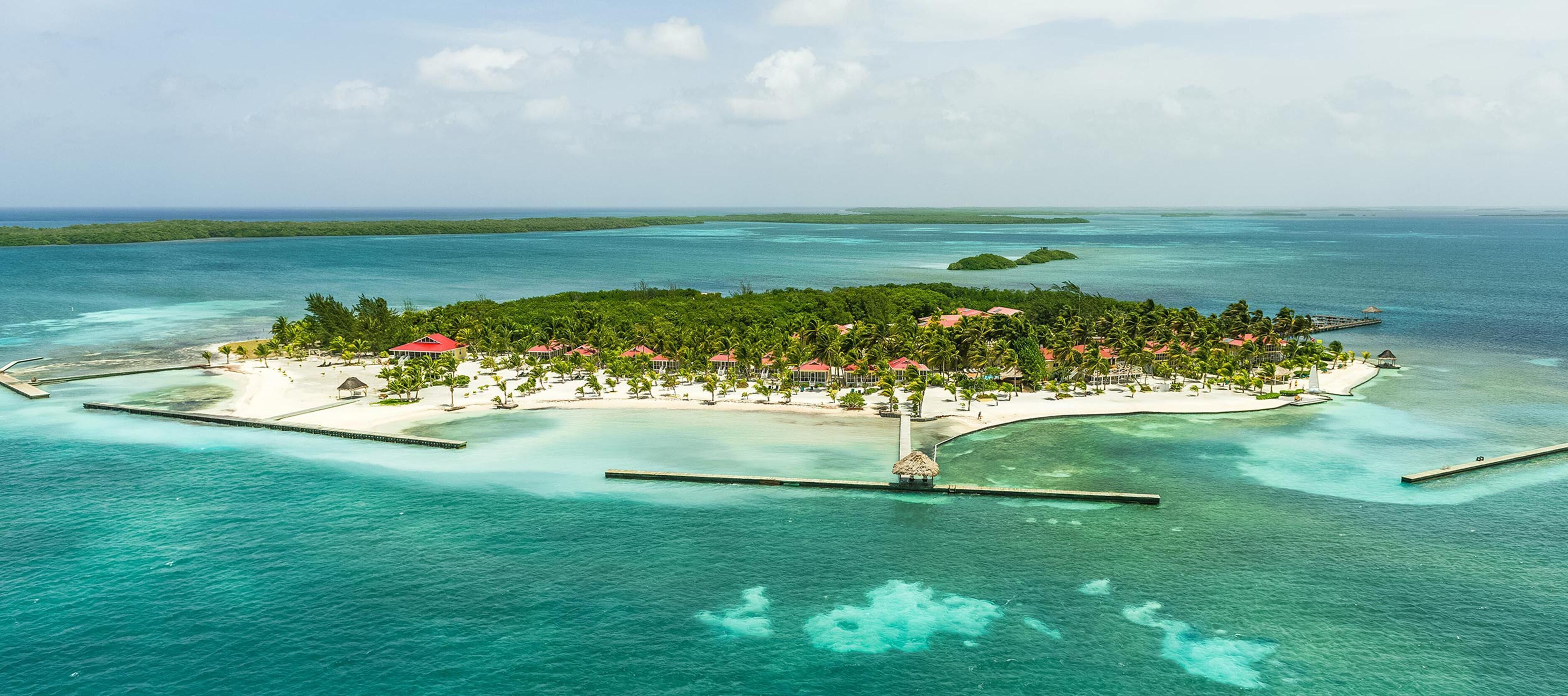Luftaufnahme eines tropischen Inselresorts mit klarem türkisfarbenem Wasser, einem Sandstrand und üppiger Vegetation.