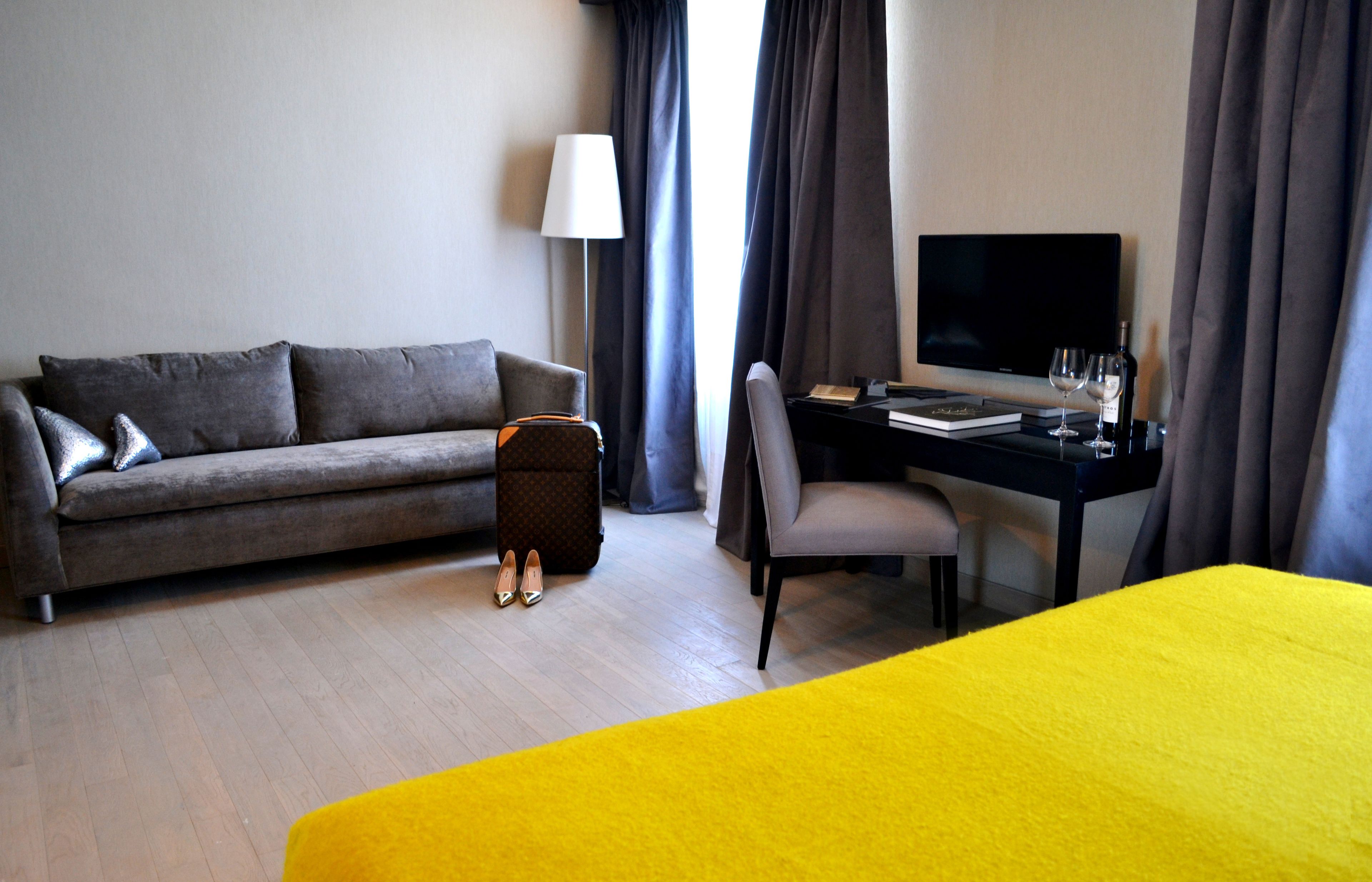 A hotel room with a sofa, a desk with a computer, a television, and a bed.