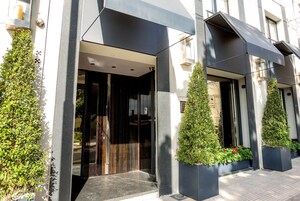 Una entrada moderna a un edificio con fachada oscura, amplias puertas de vidrio y plantas en macetas.