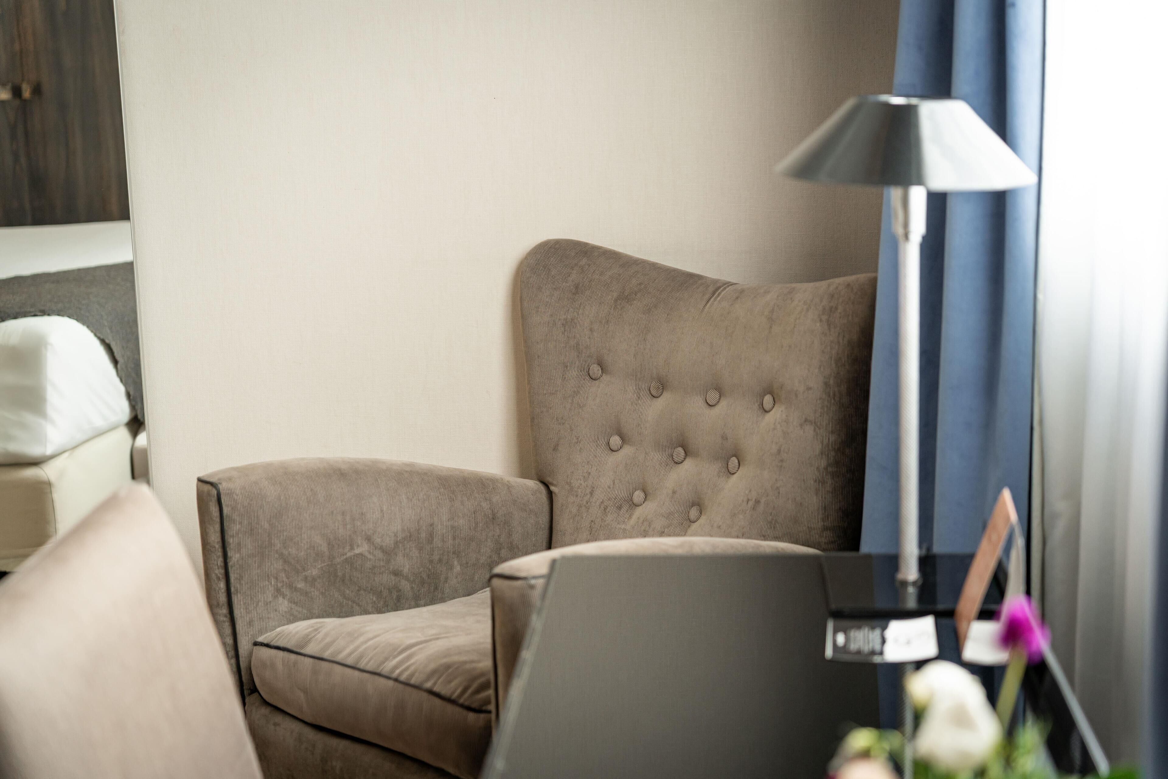 A corner of a room with a beige upholstered armchair, a matching sofa, and a floor lamp.
