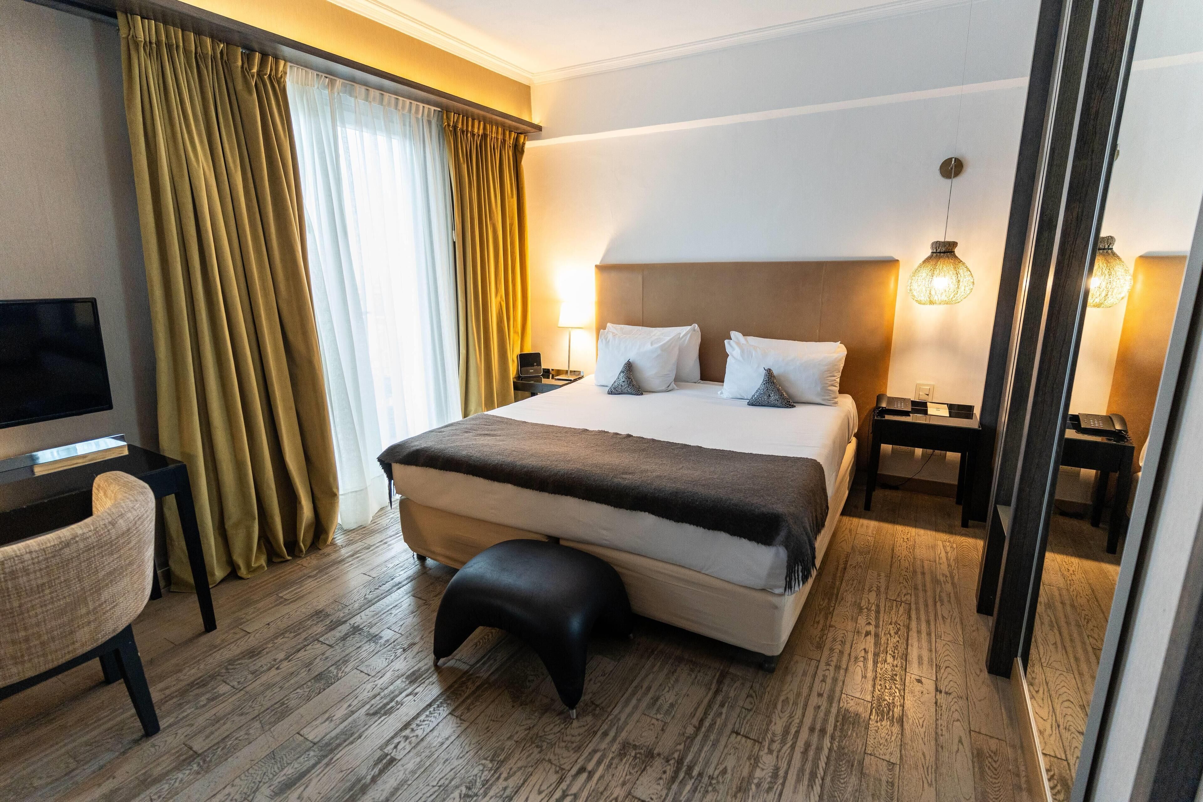A hotel room with a large bed, bedside tables, a desk, a chair, and a TV.