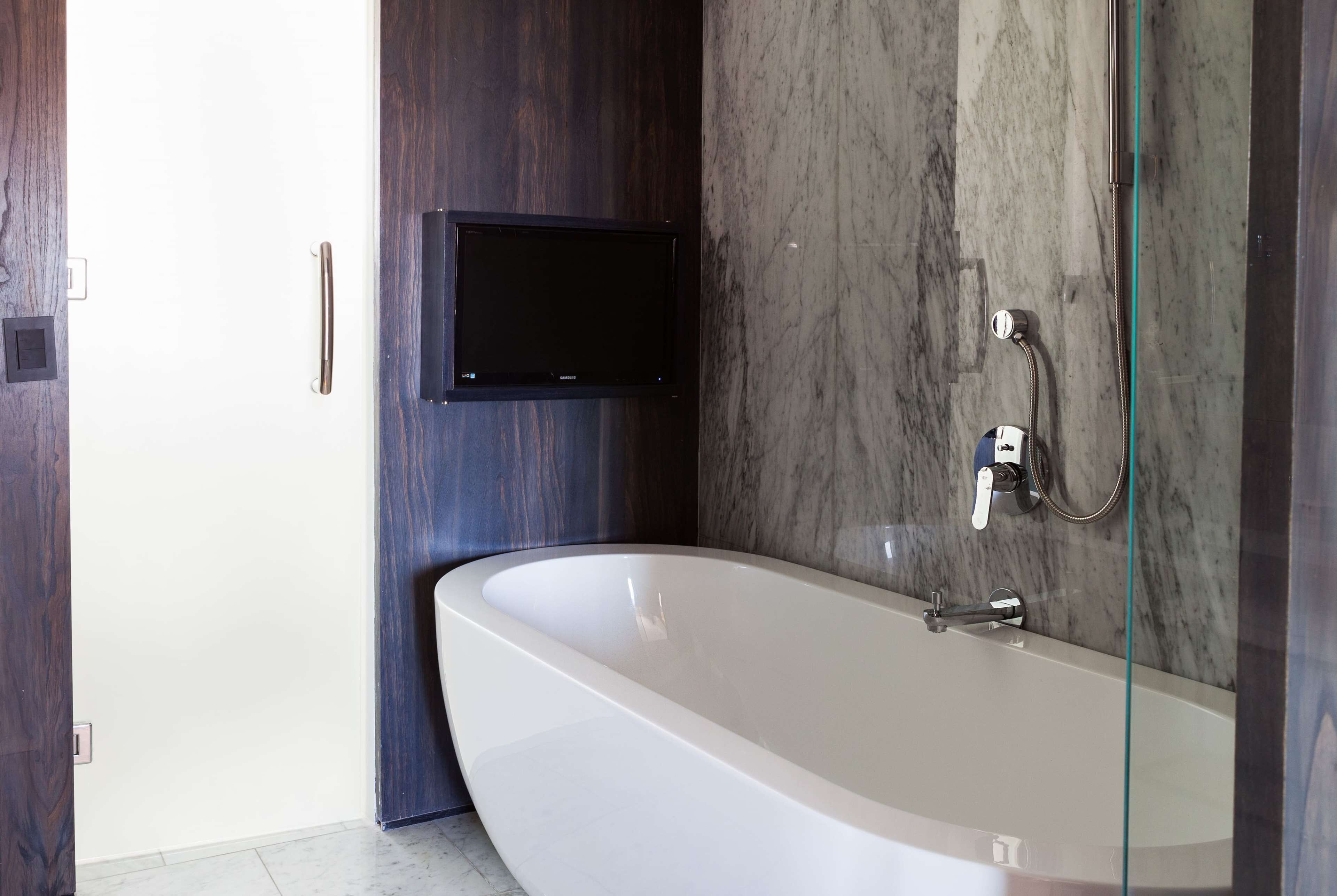A modern bathroom with a freestanding bathtub, a mounted TV, and a glass shower enclosure.
