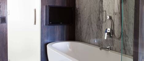 A modern bathroom with a freestanding bathtub, a mounted TV, and a glass shower enclosure.