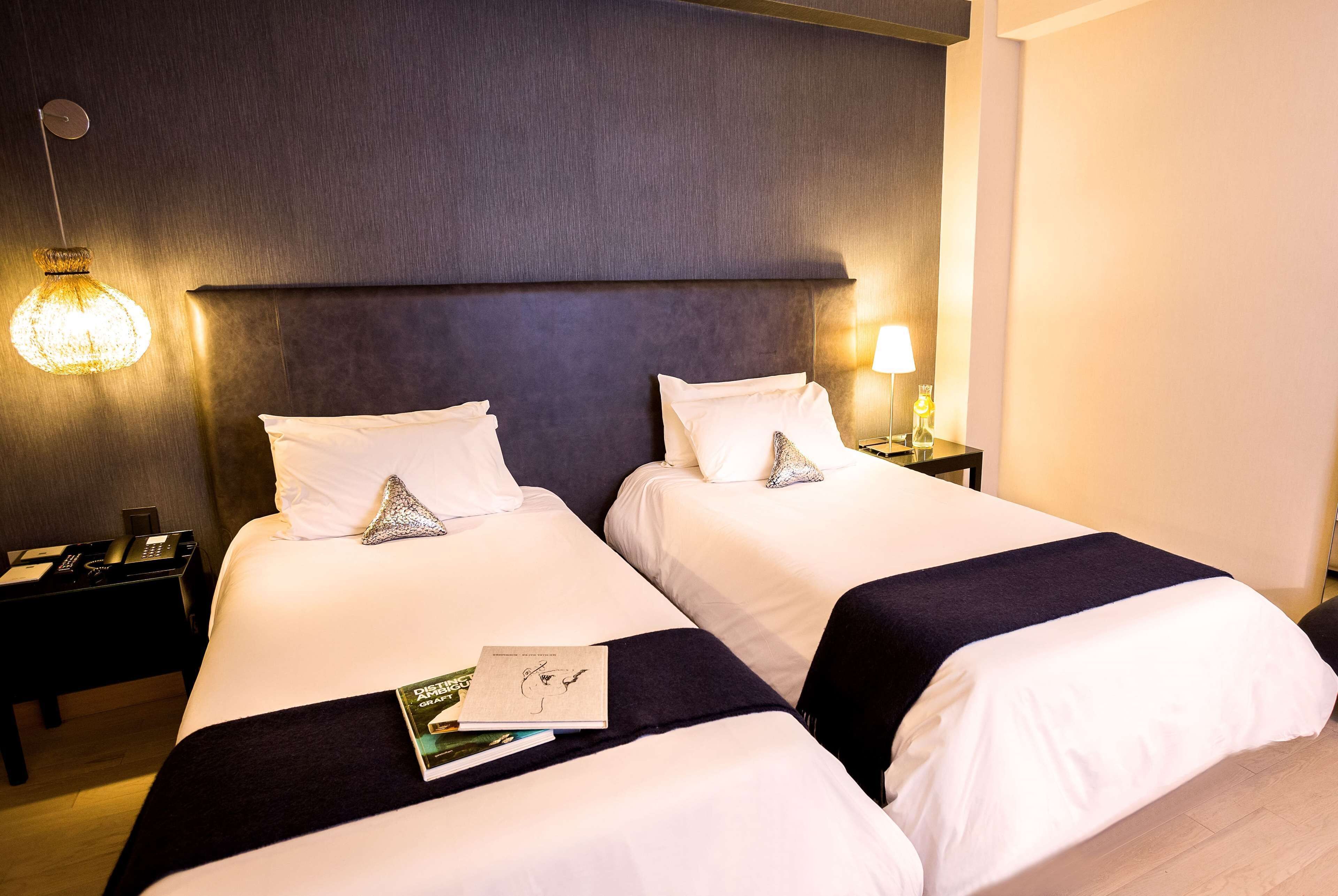 A hotel room with two beds, each with white linens and a dark headboard. There is a lamp on the right side of the room, and a book is placed on the left bed.