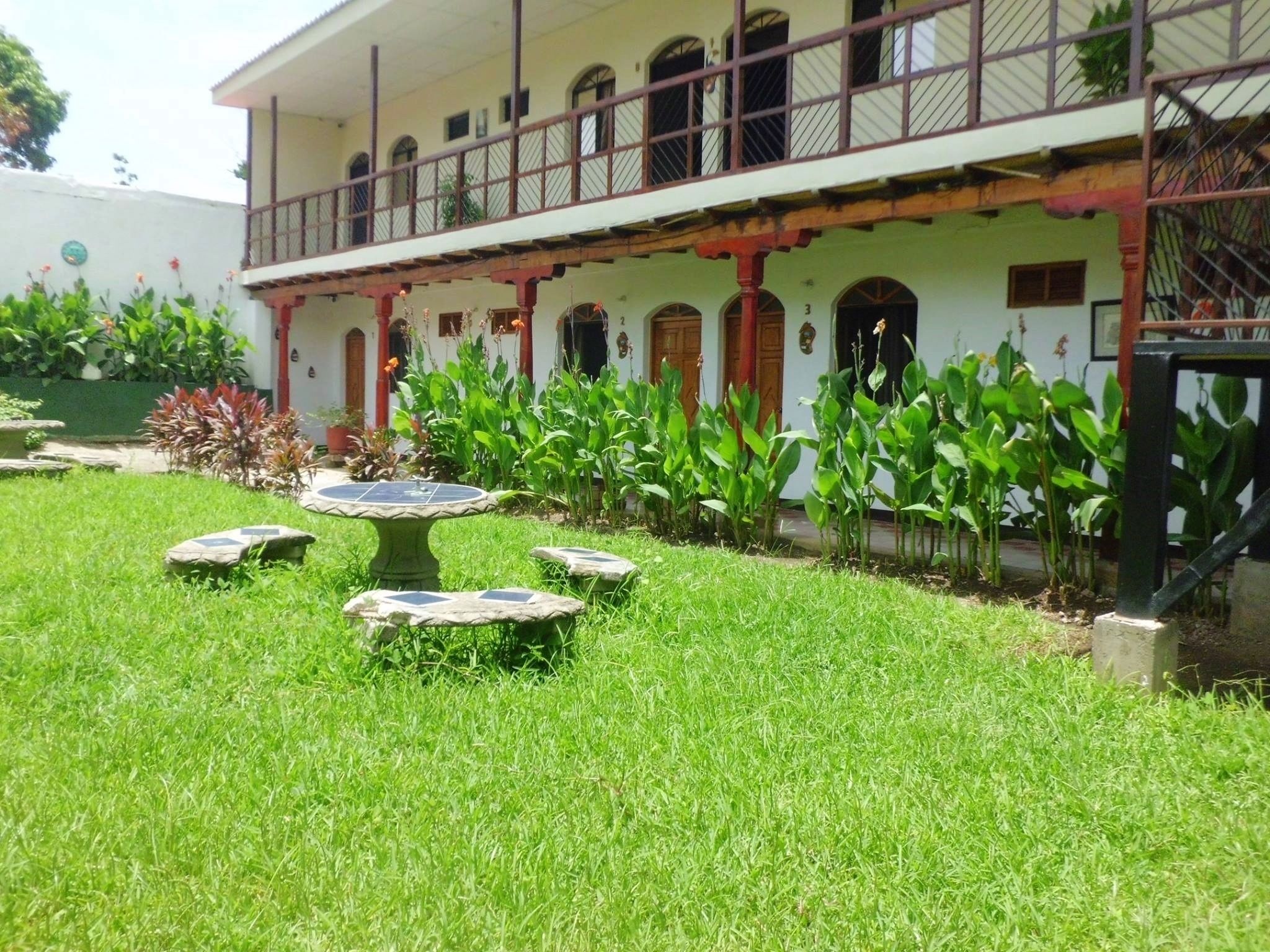 A building with a covered patio area, multiple windows, and a garden with grass and potted plants.