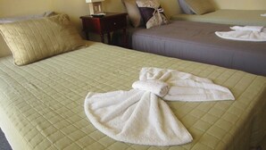 Ein Hotelzimmer mit zwei Betten, jeweils mit gesteppter Bettdecke und Kissen. An einem Nachttisch steht eine Lampe, an einem kleinen Tisch Teller und Tasse.