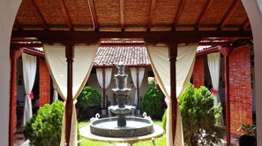Un espace extérieur abrité, doté d’une fontaine centrale, entouré de verdure et surmonté d’un toit en tuiles.