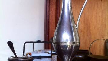 A silver pitcher with a handle, a small metal container with a spoon, and a glass on a wooden surface.