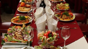 Una mesa de restaurante dispuesta con varios platos de comida, copas de vino y cubiertos.