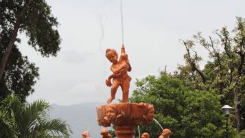 Una fuente de varios niveles con estatuas, rodeada de follaje y un cielo despejado.