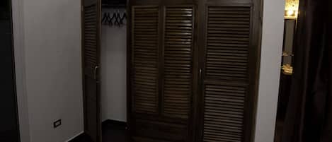 A room with a dark wooden wardrobe, a tiled floor, and a wall-mounted light fixture.