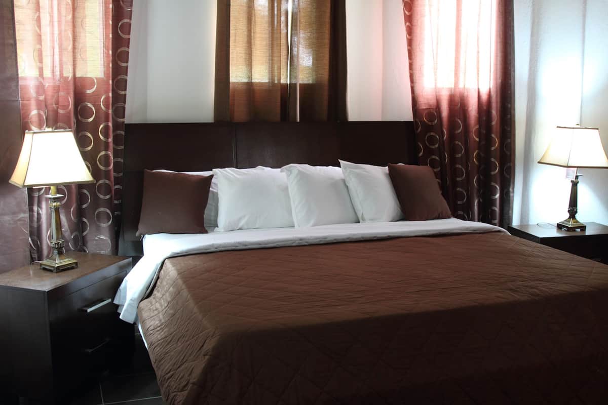 A hotel room with a large bed, two bedside tables with lamps, and curtains.