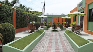 Un patio con senderos de ladrillo, macetas verdes y sillas de madera bajo sombrillas.