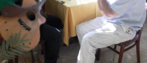 A man playing a guitar at a table with another man seated across from him.