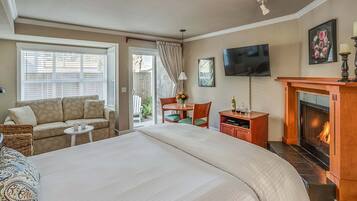 Habitación de hotel con una cama grande, un sofá, una mesita con sillas, un televisor, una chimenea y una ventana con persianas.