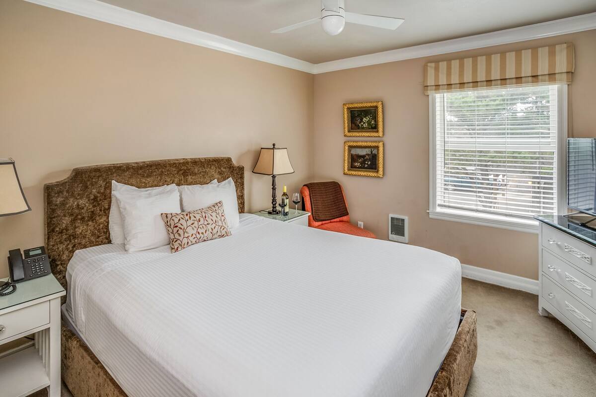 A neatly arranged bedroom with a large bed, bedside table, lamp, and a chair.