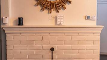 A fireplace with a brick mantel, a mirror, and a thermostat on the wall.