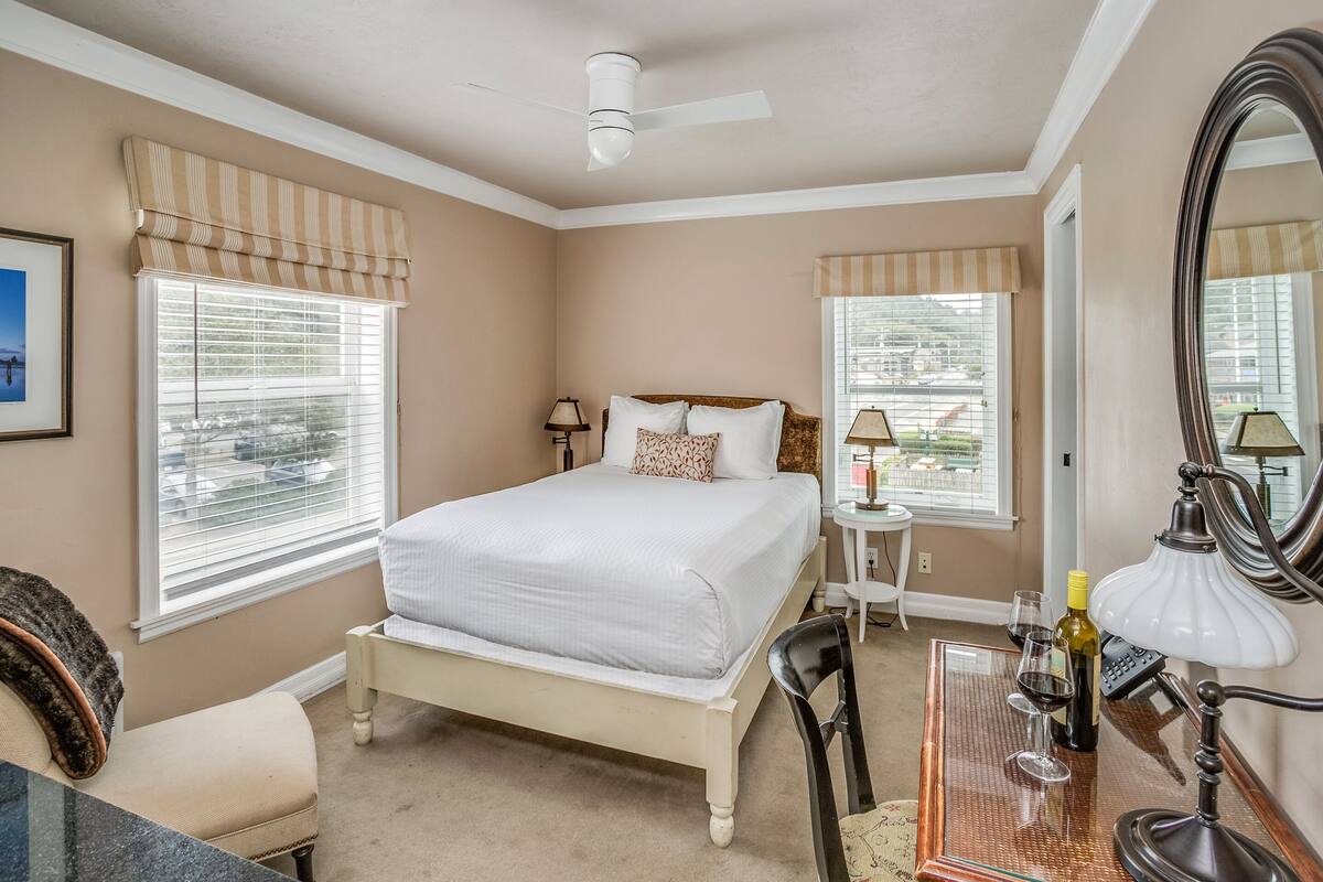 A bedroom with a bed, bedside tables, a desk with a lamp, and a large mirror.