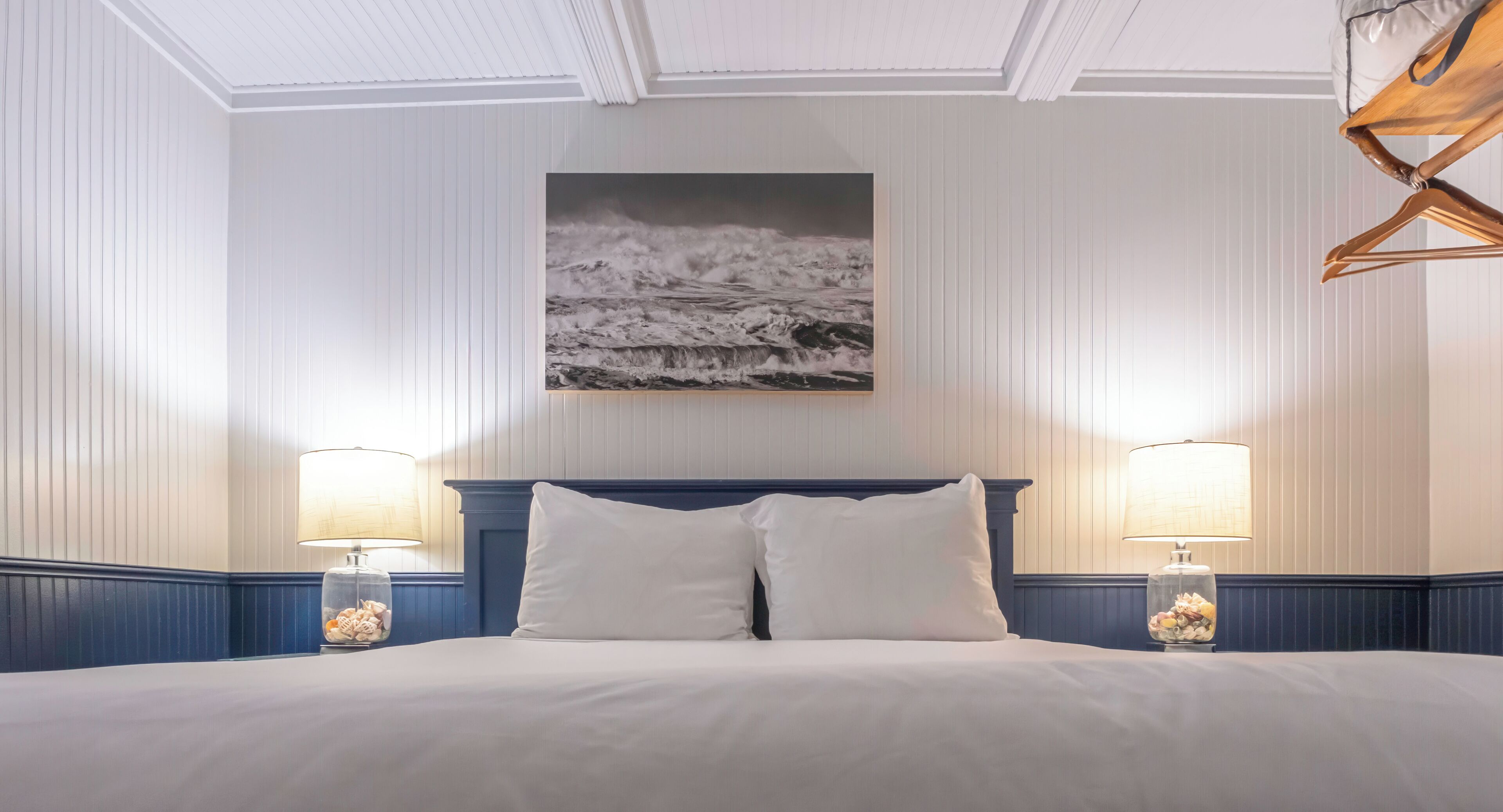 A hotel room with a bed, two bedside lamps, a framed picture on the wall, and a ceiling with a decorative design.