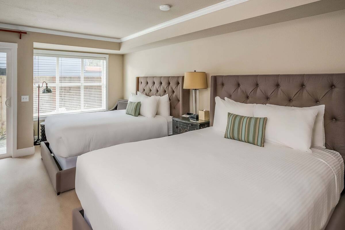 A hotel room with two beds, a nightstand with a lamp, and a window with blinds.