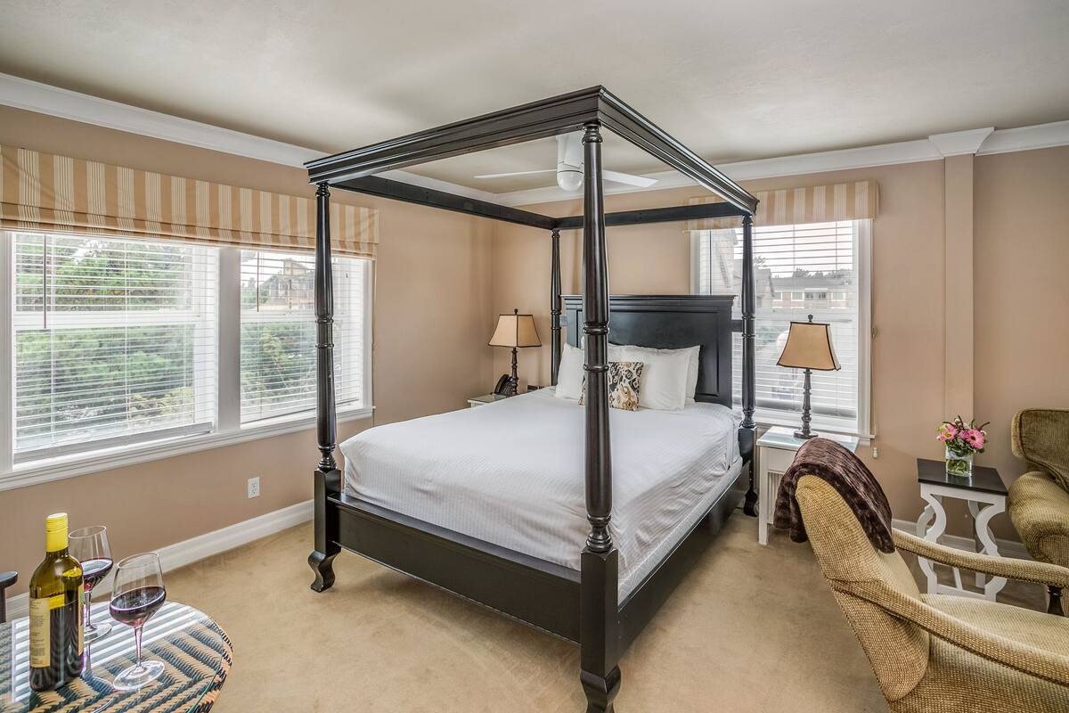 A four-poster bed in a room with beige walls and large windows.