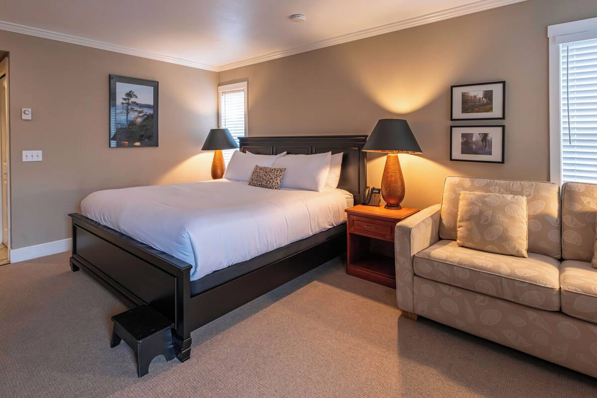 A bedroom with a bed, bedside lamps, a nightstand, a sofa, and wall-mounted pictures.
