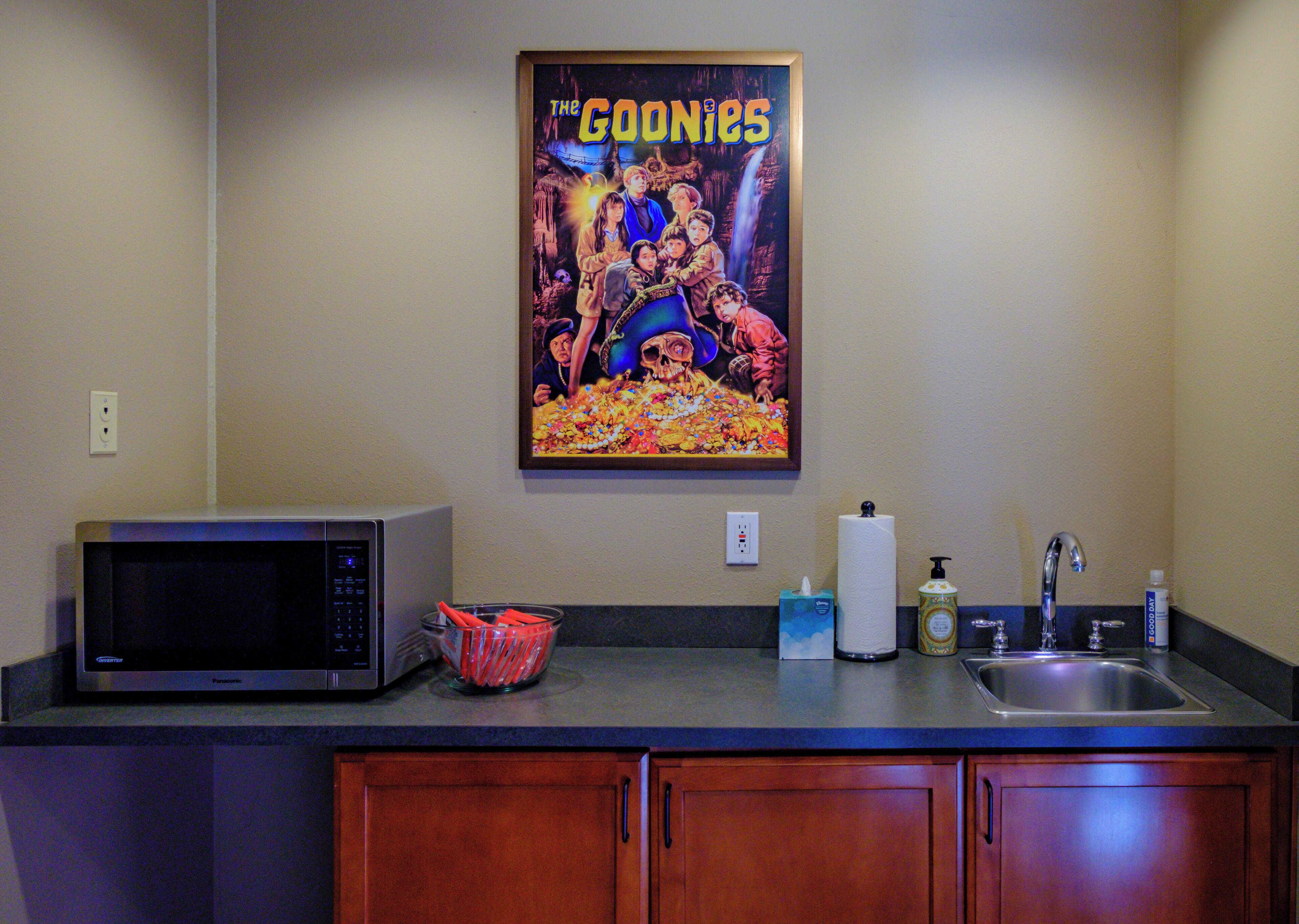 A kitchen with a microwave, a sink, and a poster of 'The Goonies' on the wall.
