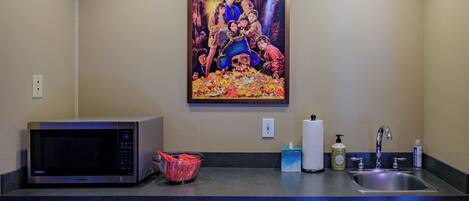 A kitchen with a microwave, a sink, and a poster of 'The Goonies' on the wall.
