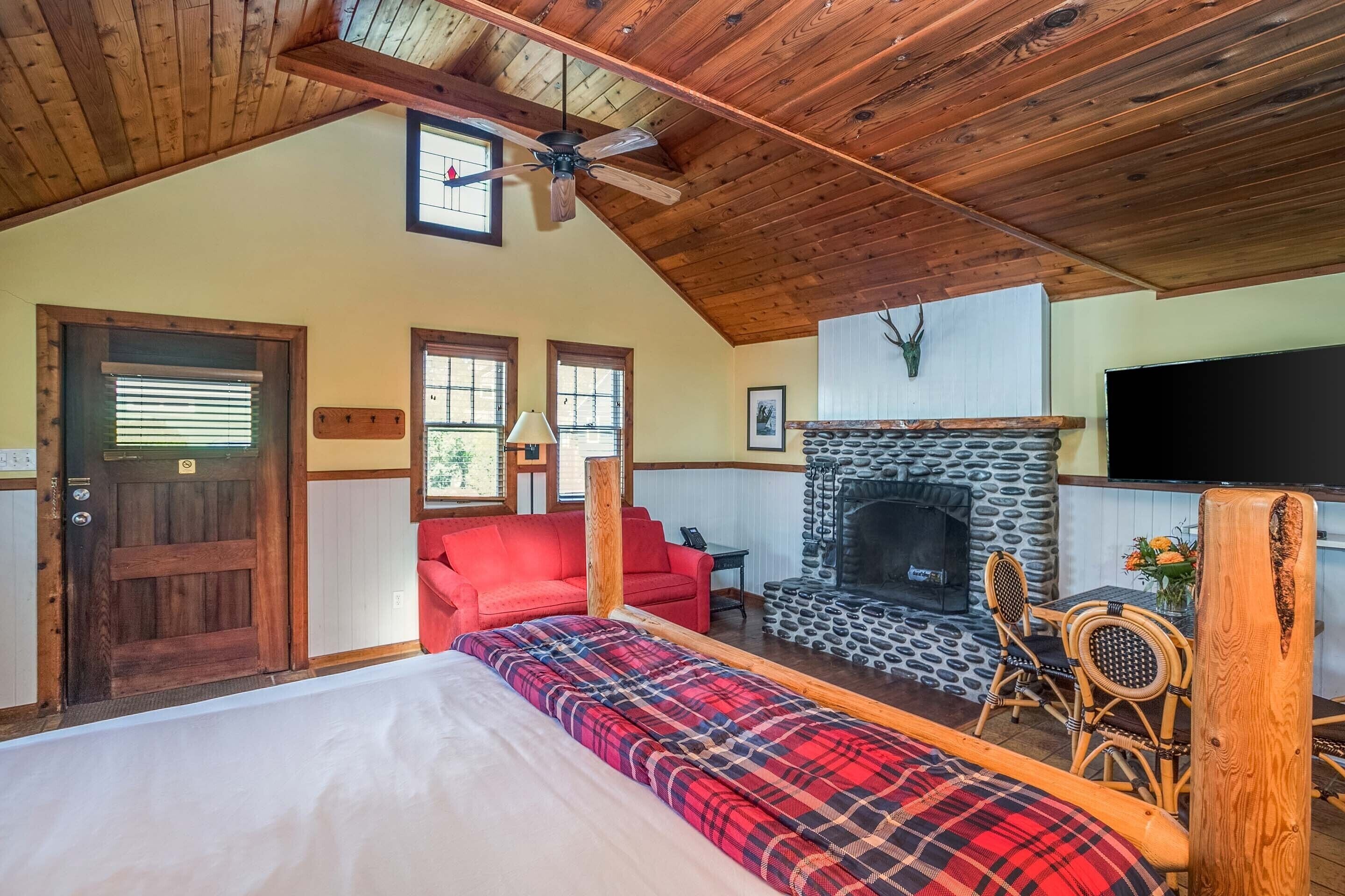 Una habitación acogedora con cama, chimenea, un sofá rojo y un comedor con mesa y sillas.