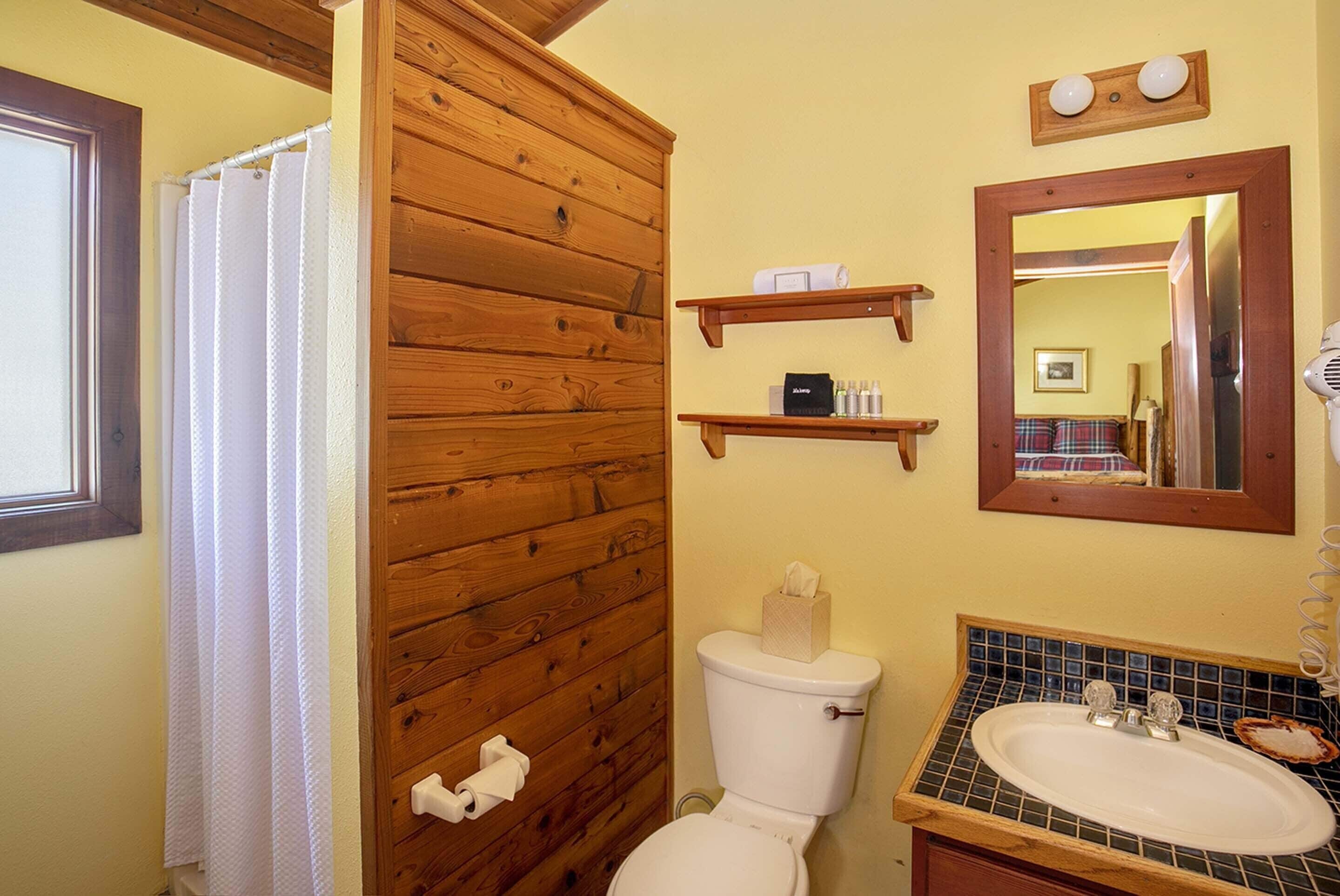 Un baño con paneles de madera, un inodoro, un lavabo con salpicadero de azulejos y un espejo sobre el lavabo.