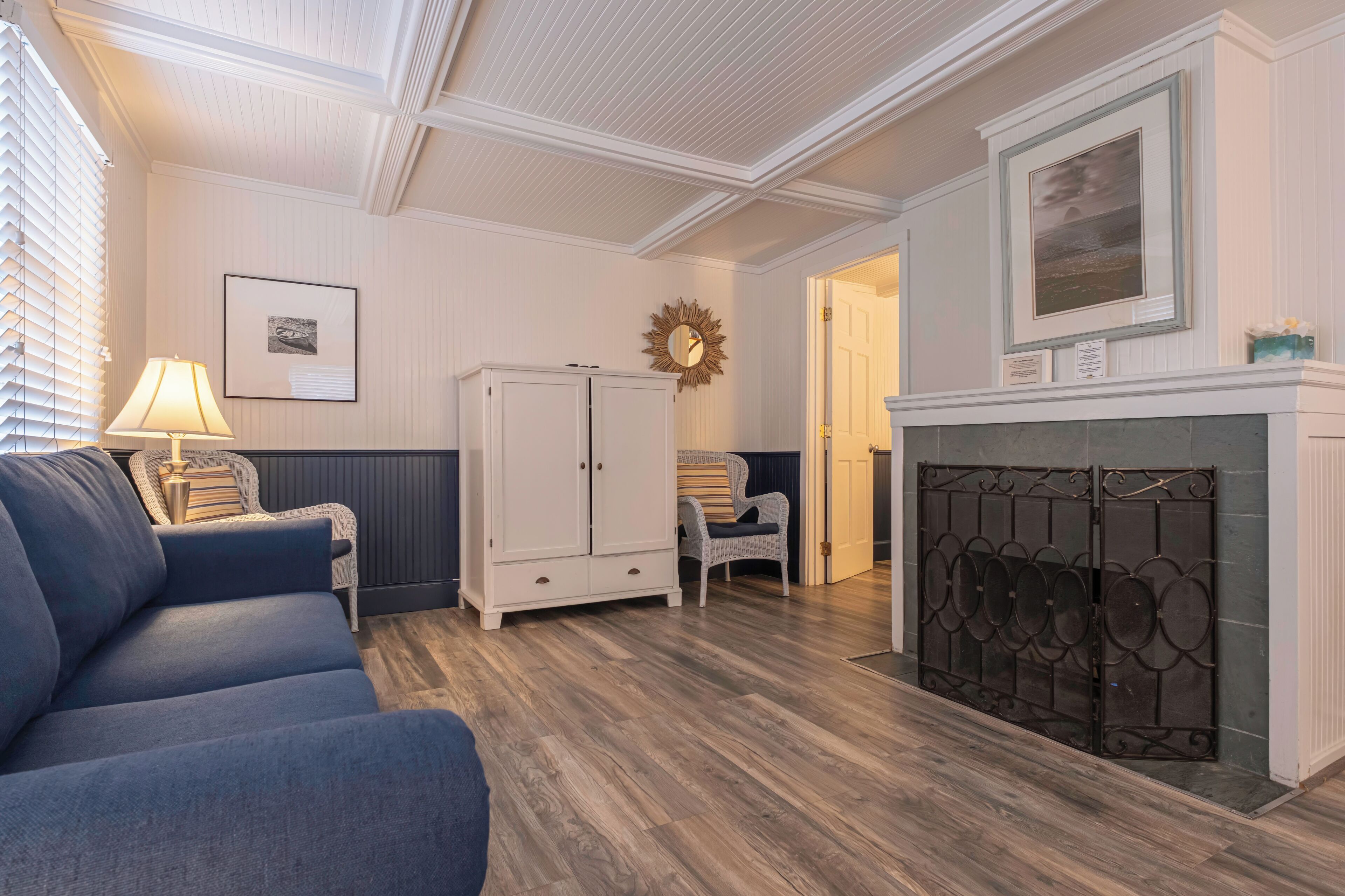 A room with a blue sofa, a white cabinet, a fireplace, and a framed picture on the wall.