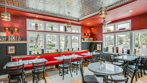 Un ristorante con pareti rosse, ampie finestre e diverse opzioni di posti a sedere, tra cui tavoli e panche.