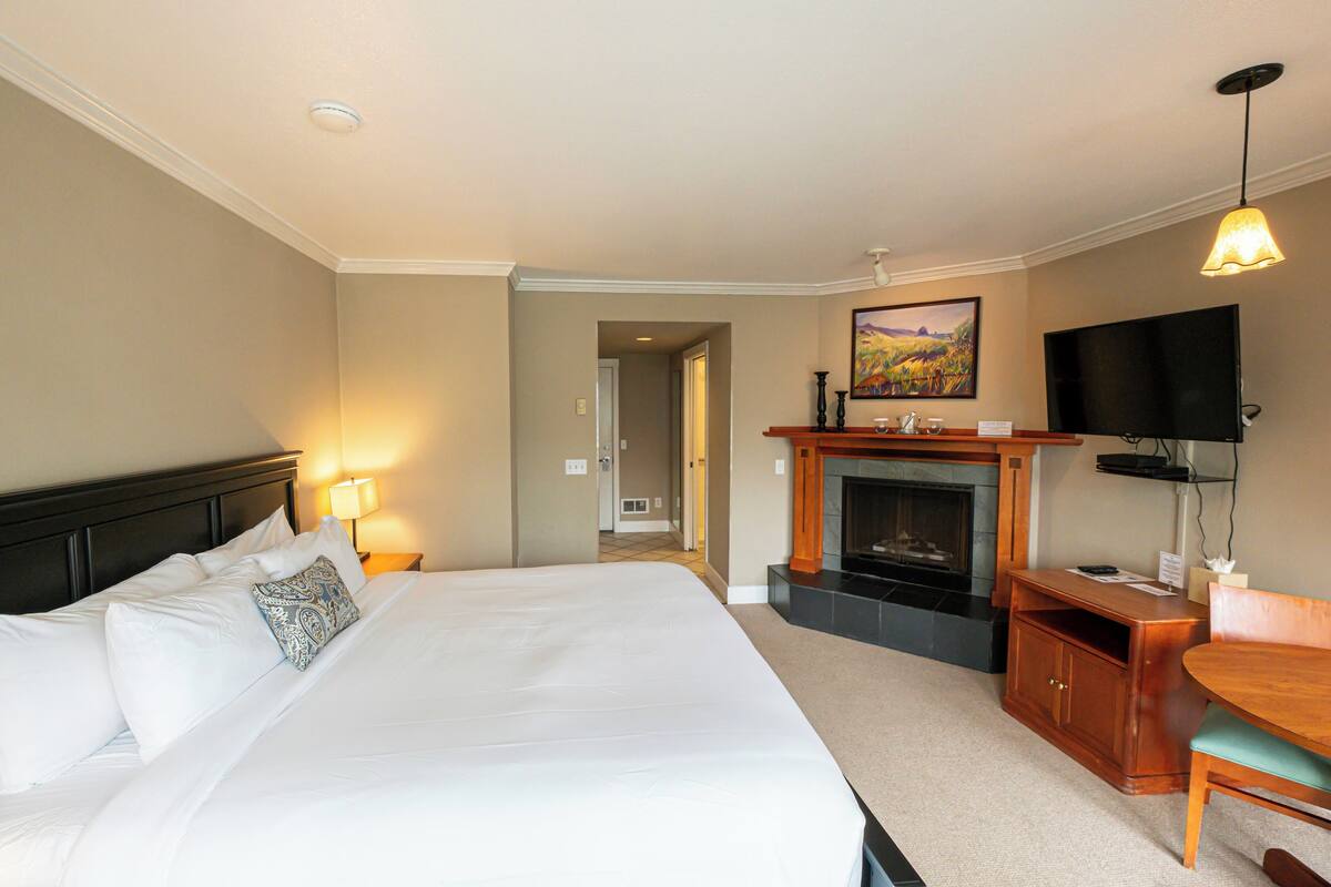 A hotel room with a large bed, a fireplace, a television, and a desk with a chair.