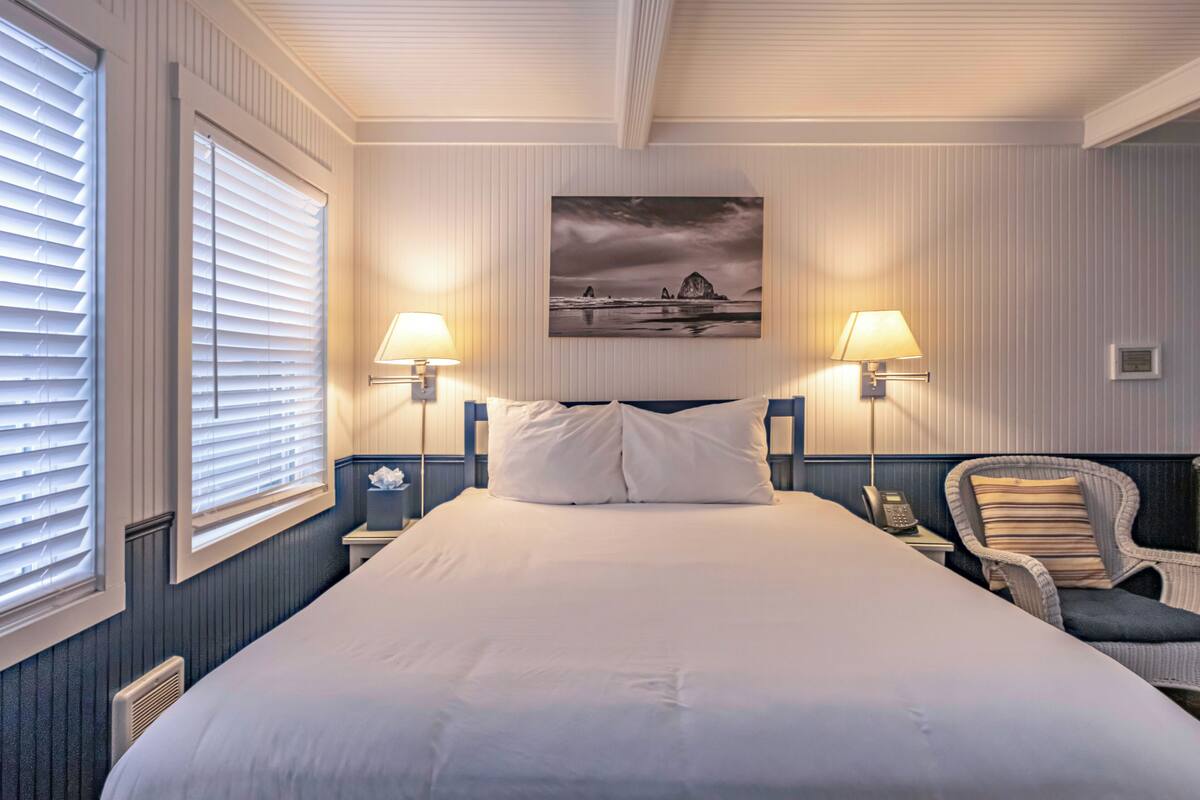A hotel room with a large bed, two bedside lamps, a chair, and a wall-mounted painting.