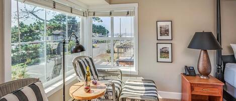 A room with wicker furniture, a wooden nightstand, and a view through large windows.