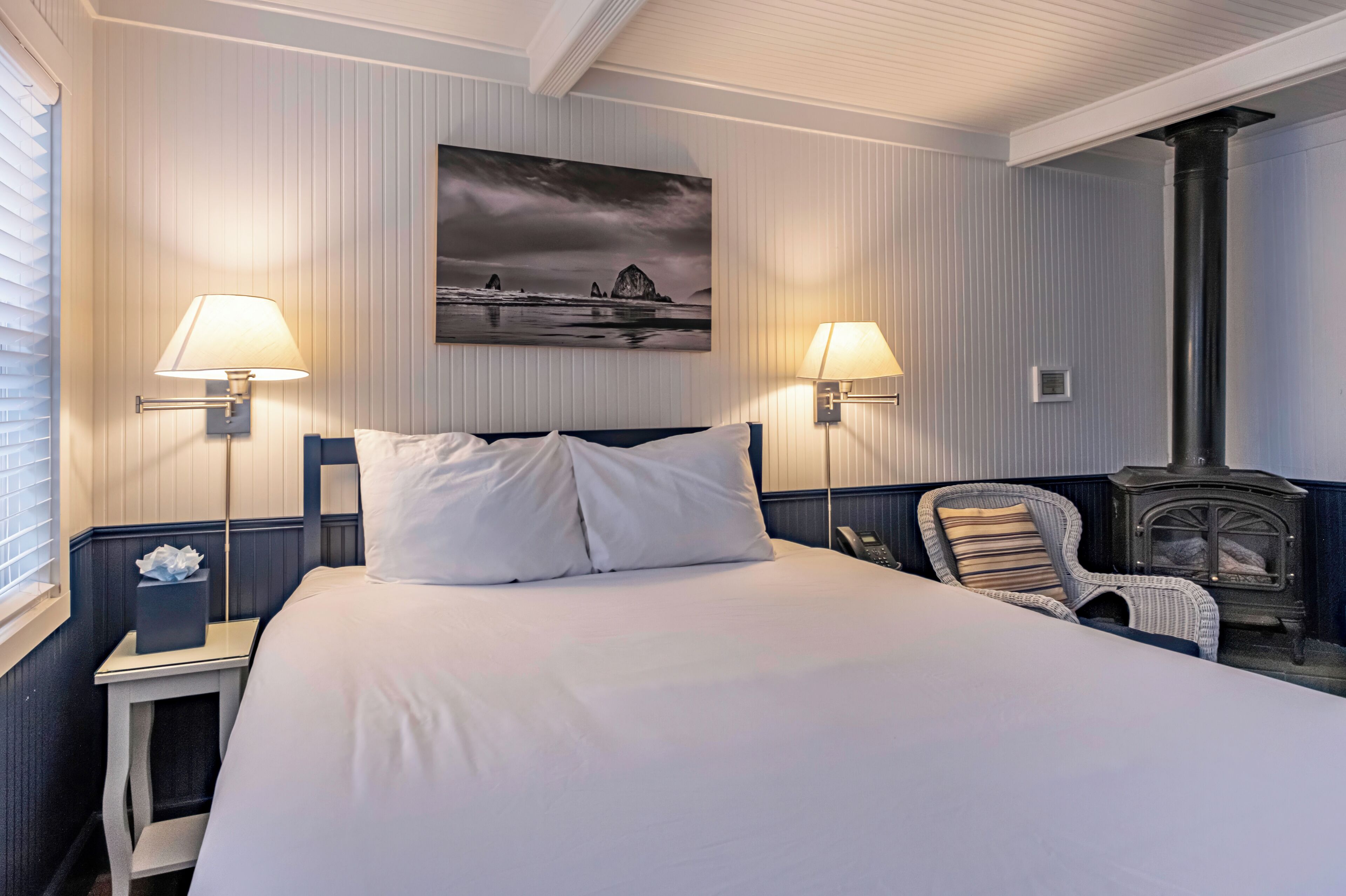 Een hotelkamer met een bed, twee bedlampen, een stoel, een schilderij en een houtkachel.