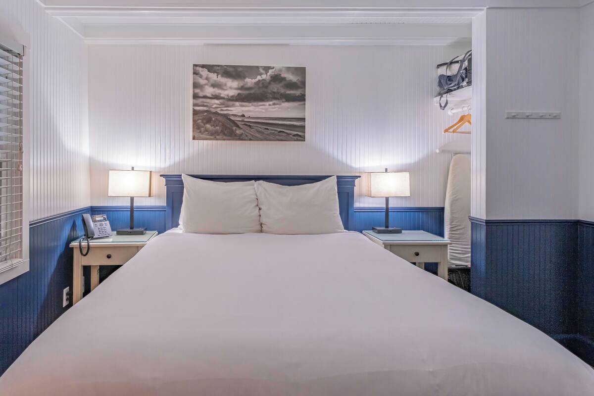 A hotel room with a large bed, two bedside tables with lamps, a painting on the wall, and a wardrobe.