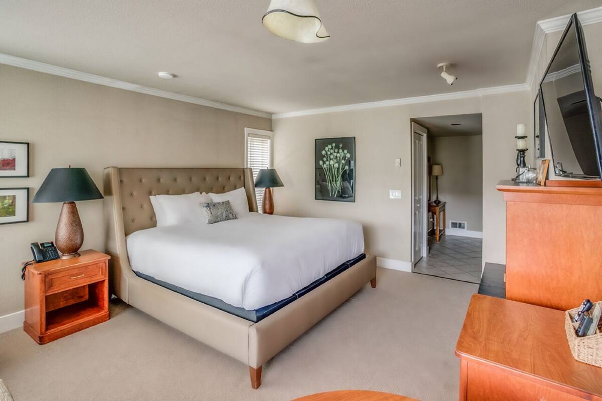 A bedroom with a large bed, two bedside tables, a dresser, a television, and a door leading to another room.
