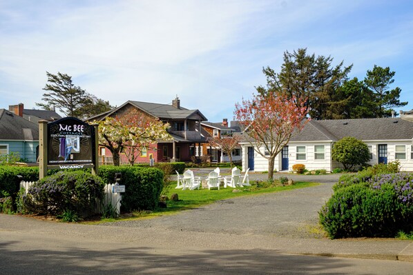 A cottage-style hotel with a signboard, a gravel driveway, and white outdoor chairs.