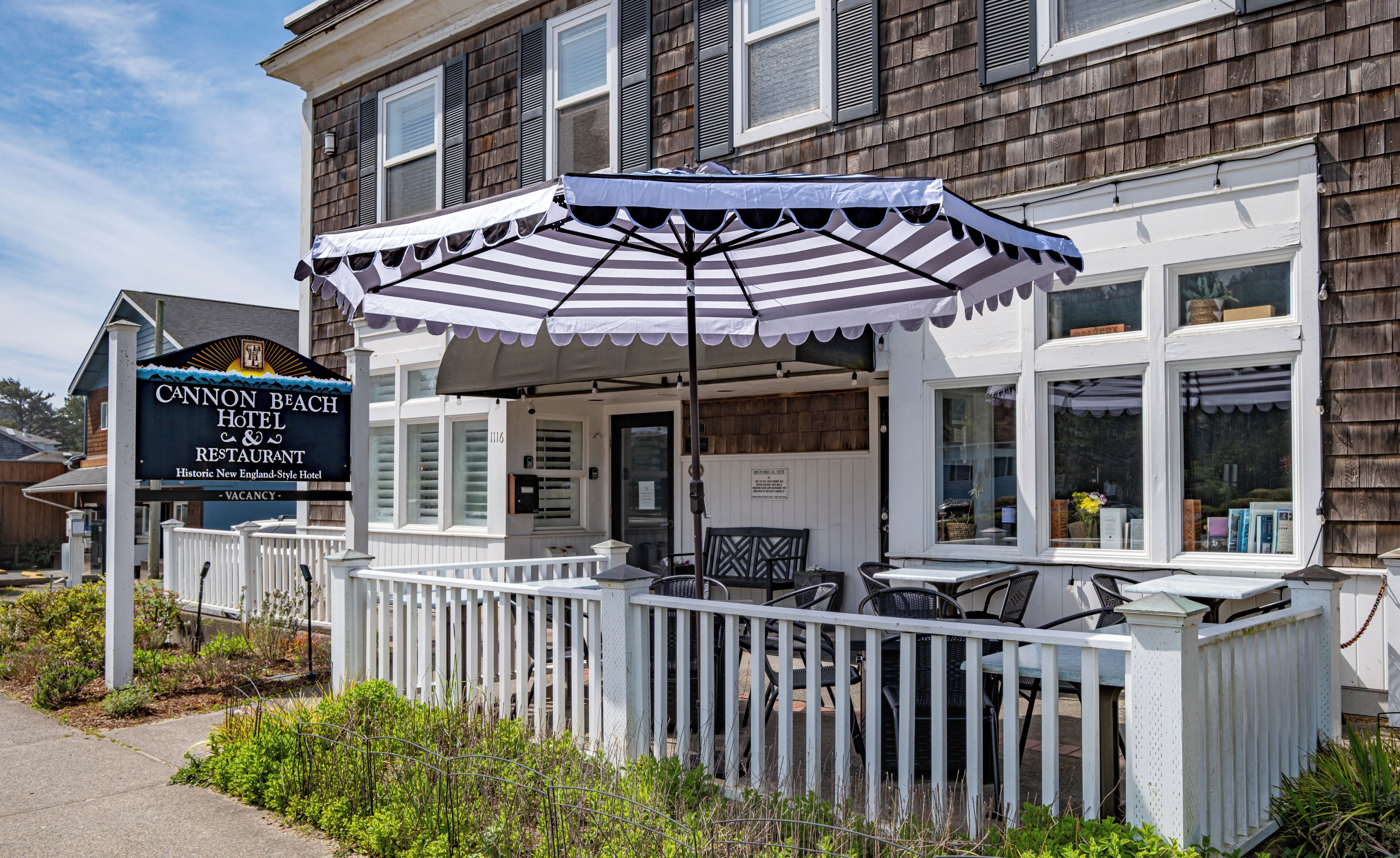 A historic New England-style hotel with a covered patio, white picket fence, and outdoor seating.