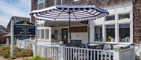 A historic New England-style hotel with a covered patio, white picket fence, and outdoor seating.