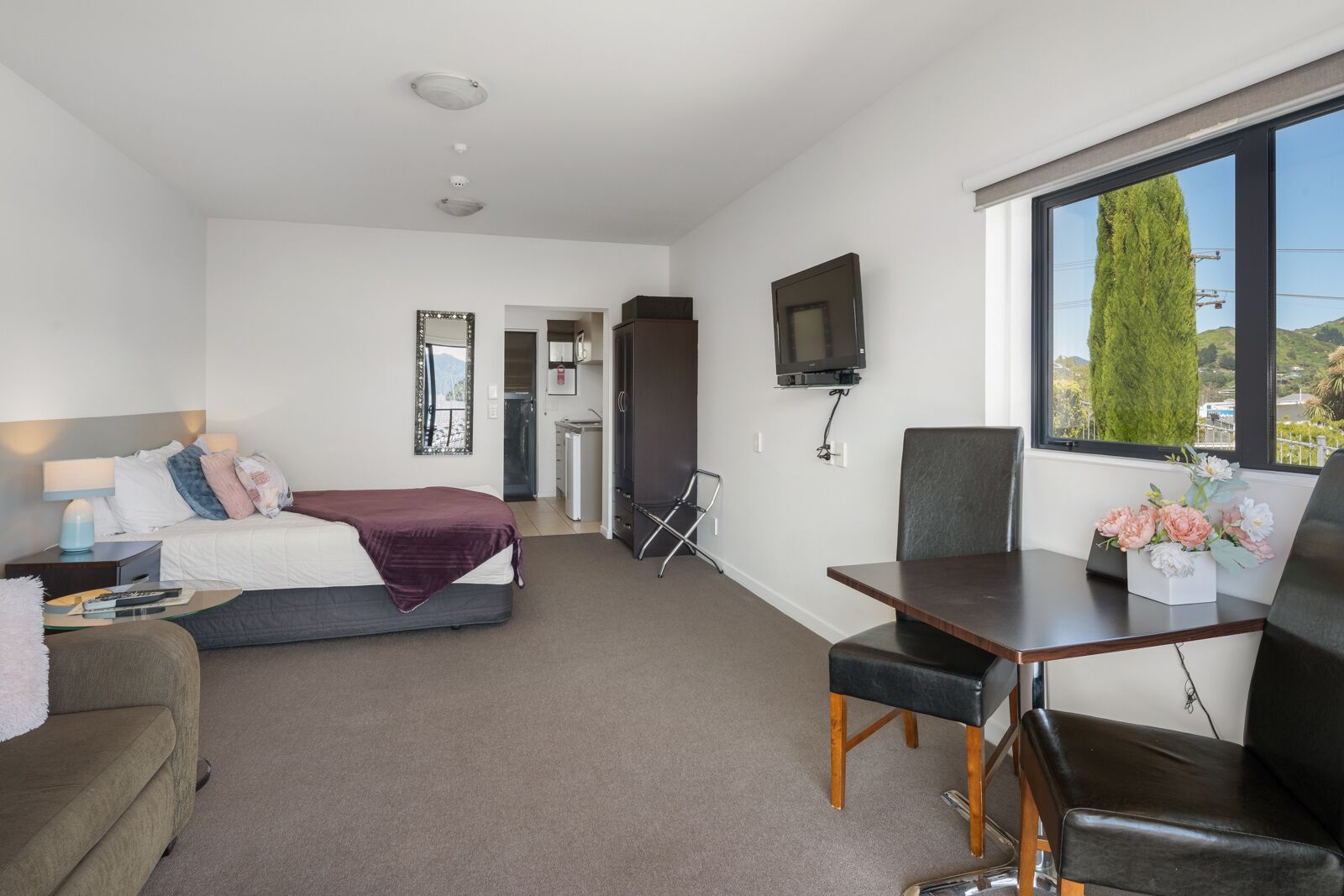 A modern hotel room with a bed, a desk, a chair, a TV, and a window with a view.