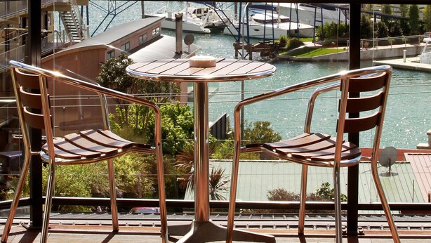 A terrace with two wooden chairs and a table, overlooking a marina with boats and a cruise ship in the background. - Harbour View Motel (Picton)