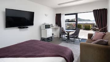 Une chambre d’hôtel comprenant un lit, une télévision, un bureau avec une chaise, une petite kitchenette et un balcon avec des rideaux.