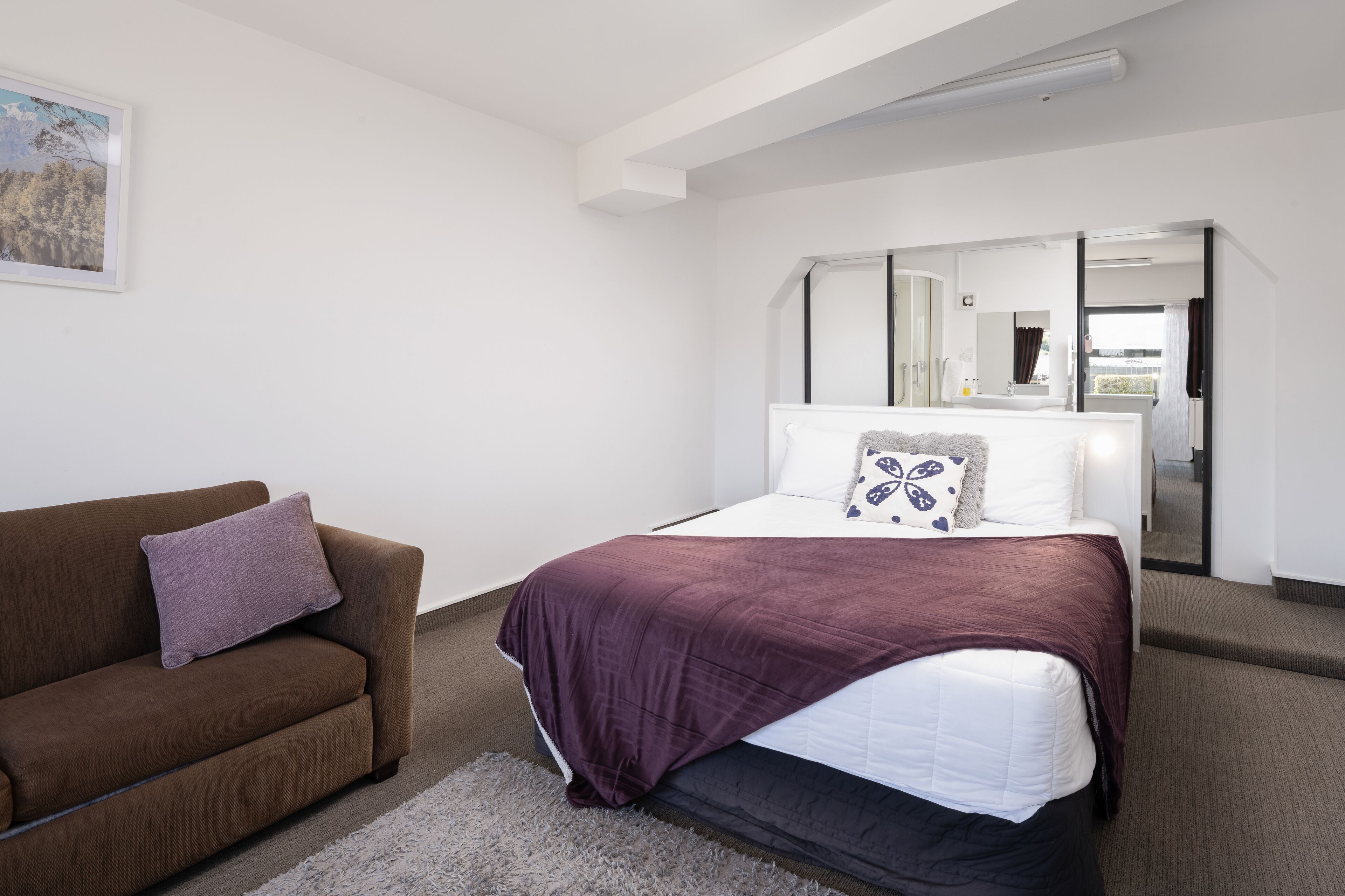 A modern bedroom with a bed, a sofa, and a large mirror.