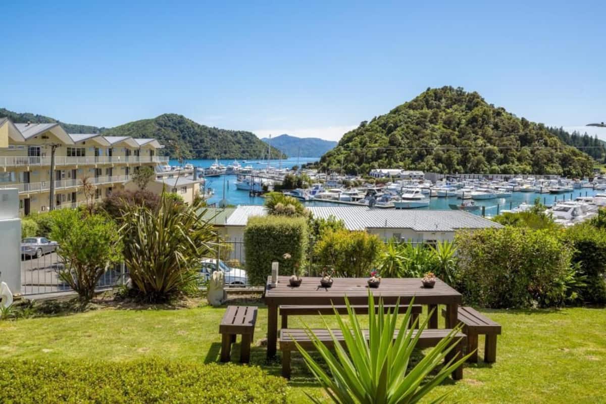 A marina with boats, a hill with dense greenery, and a building with balconies.
