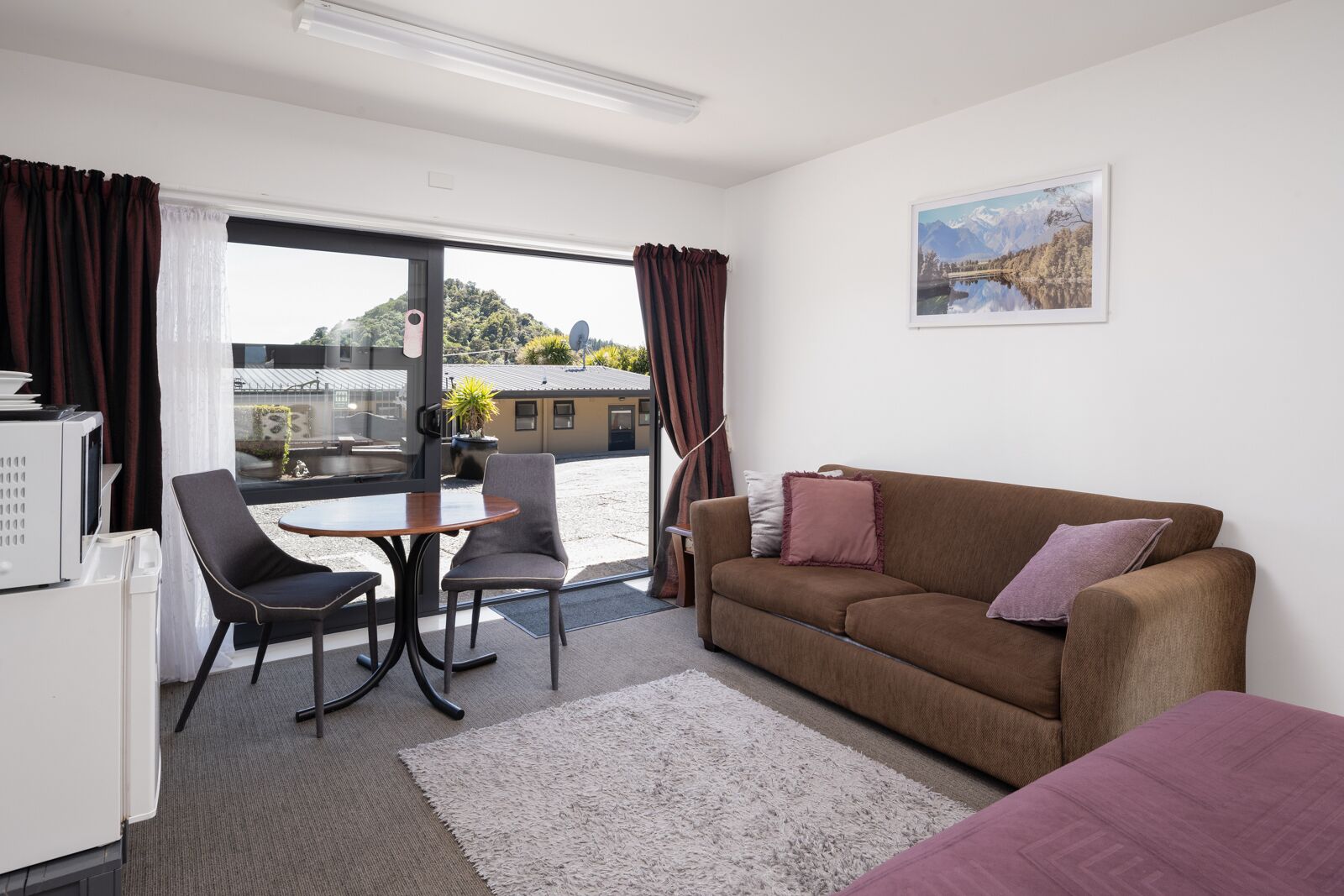 A modern living room with a brown sofa, two chairs, a small table, and a large window with curtains.