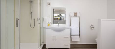 Un baño moderno con ducha de vidrio, lavabo con espejo y retrete.